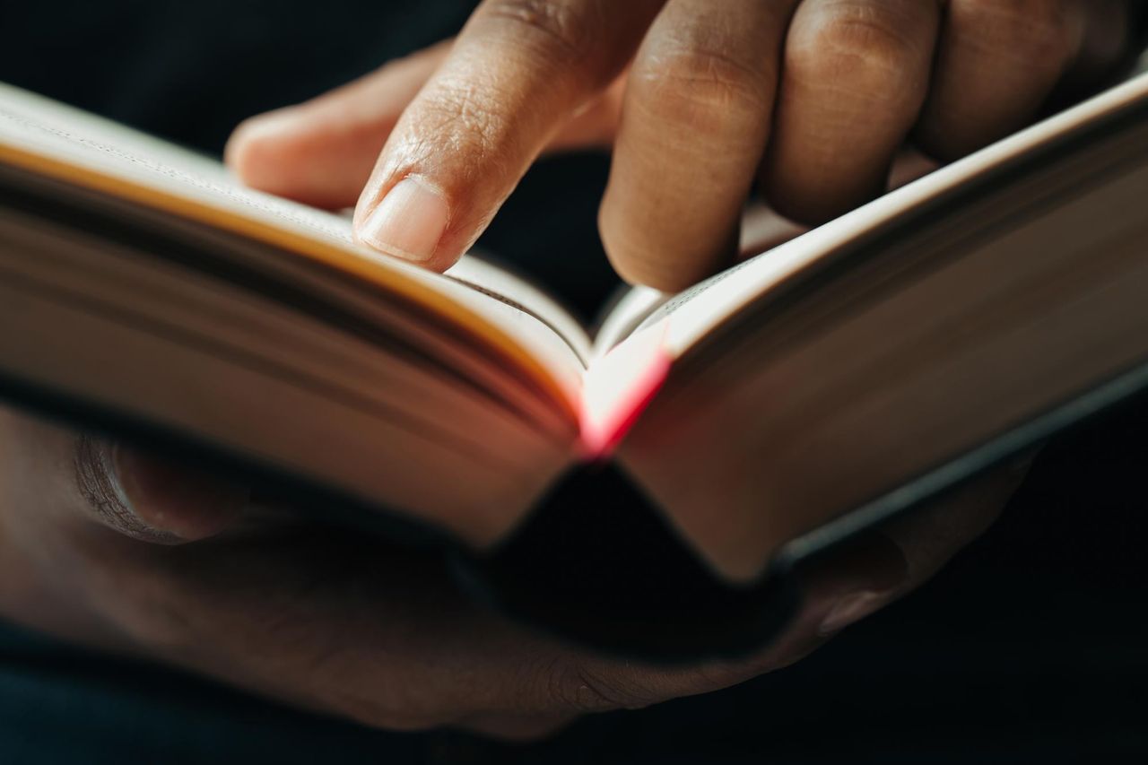 Открытая библия, человек ведет по строкам в книге и читает